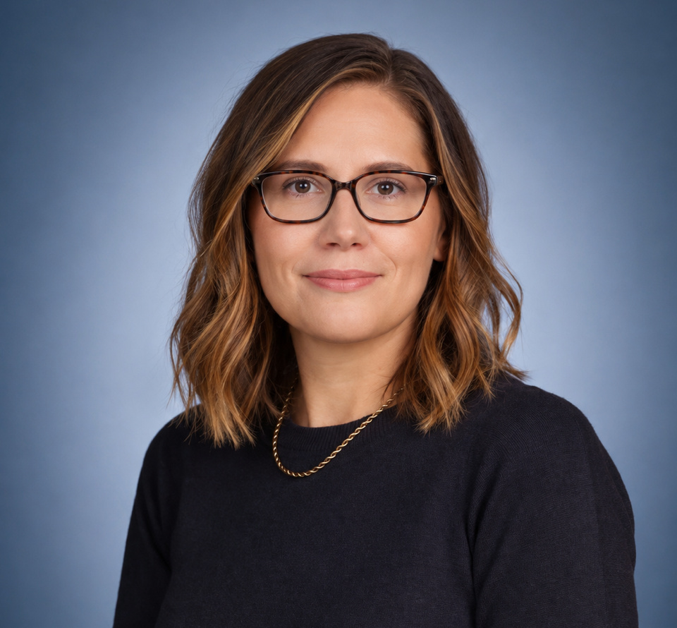 Professional headshot of a woman with glasses and shoulder-length brown hair, wearing a dark blue sweater and a gold necklace against a gradient blue background.