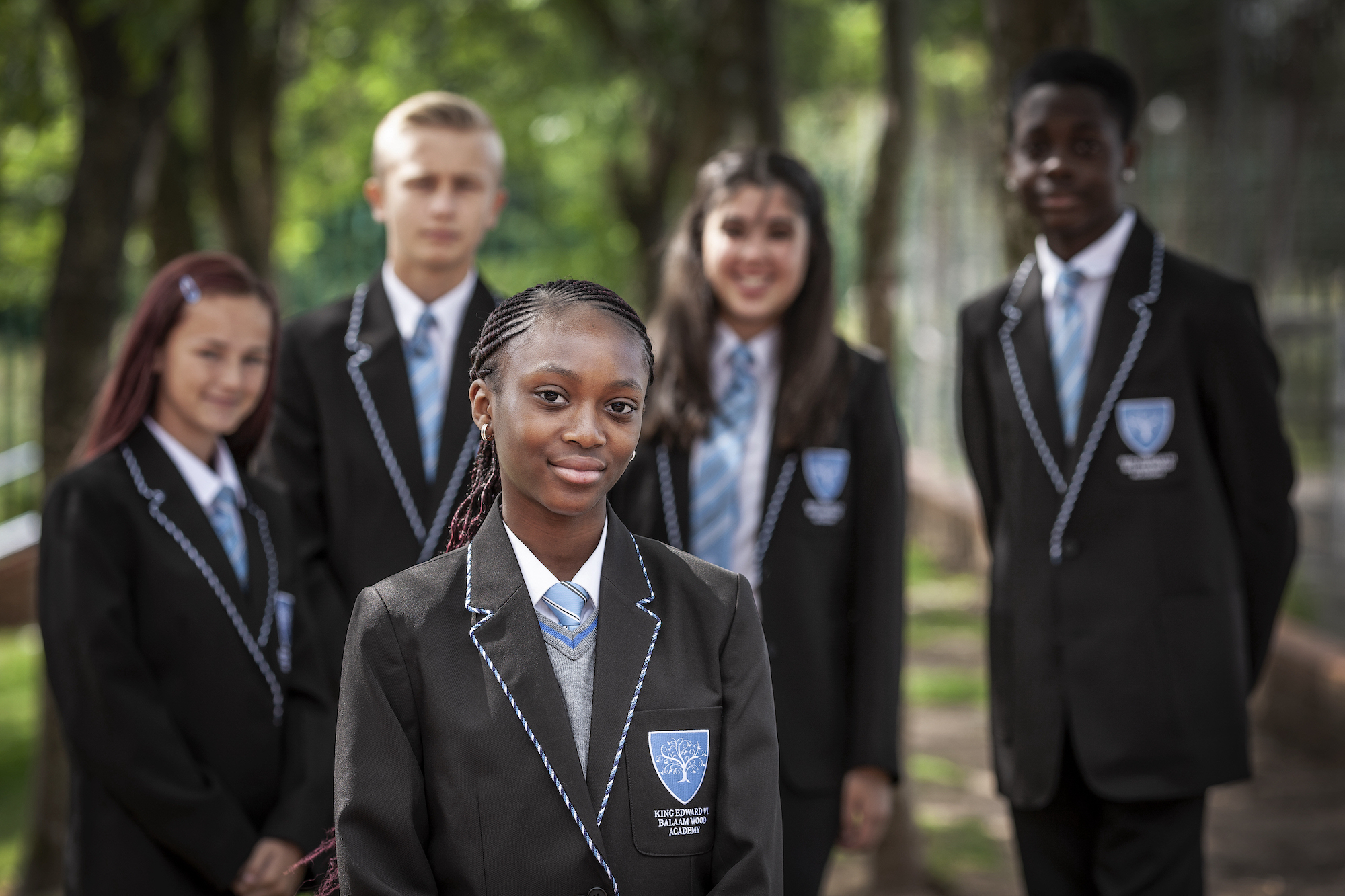 A group of students in school uniform standing outside on campus, smiling for a photo.