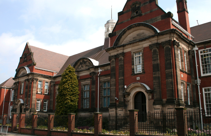 A red brick building with a brown roof, surrounded by a black fence, representing a safe and secure educational environment.