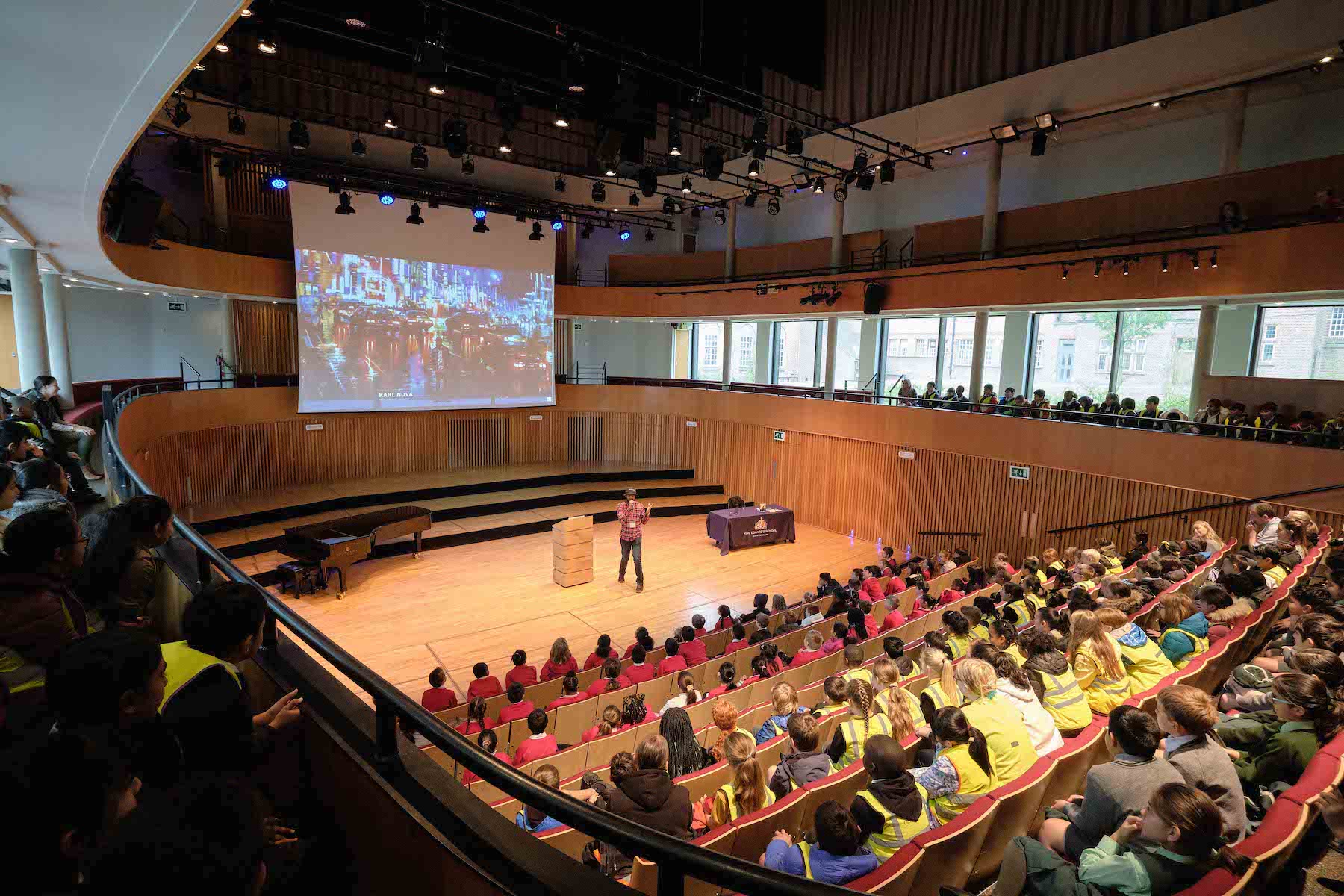 A large auditorium with students seated and a speaker on stage, engaged in an educational activity.