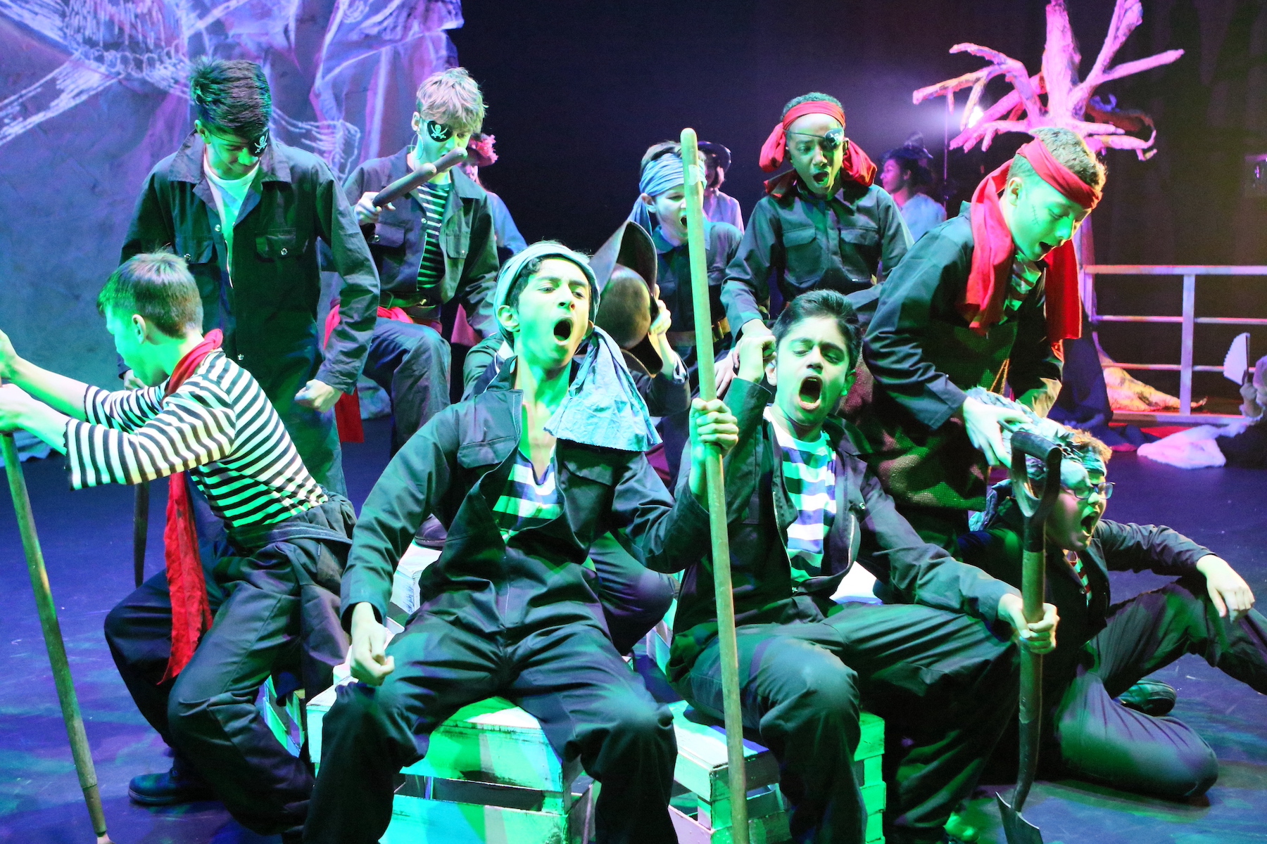 Students performing on stage with expressive gestures and colourful lighting.