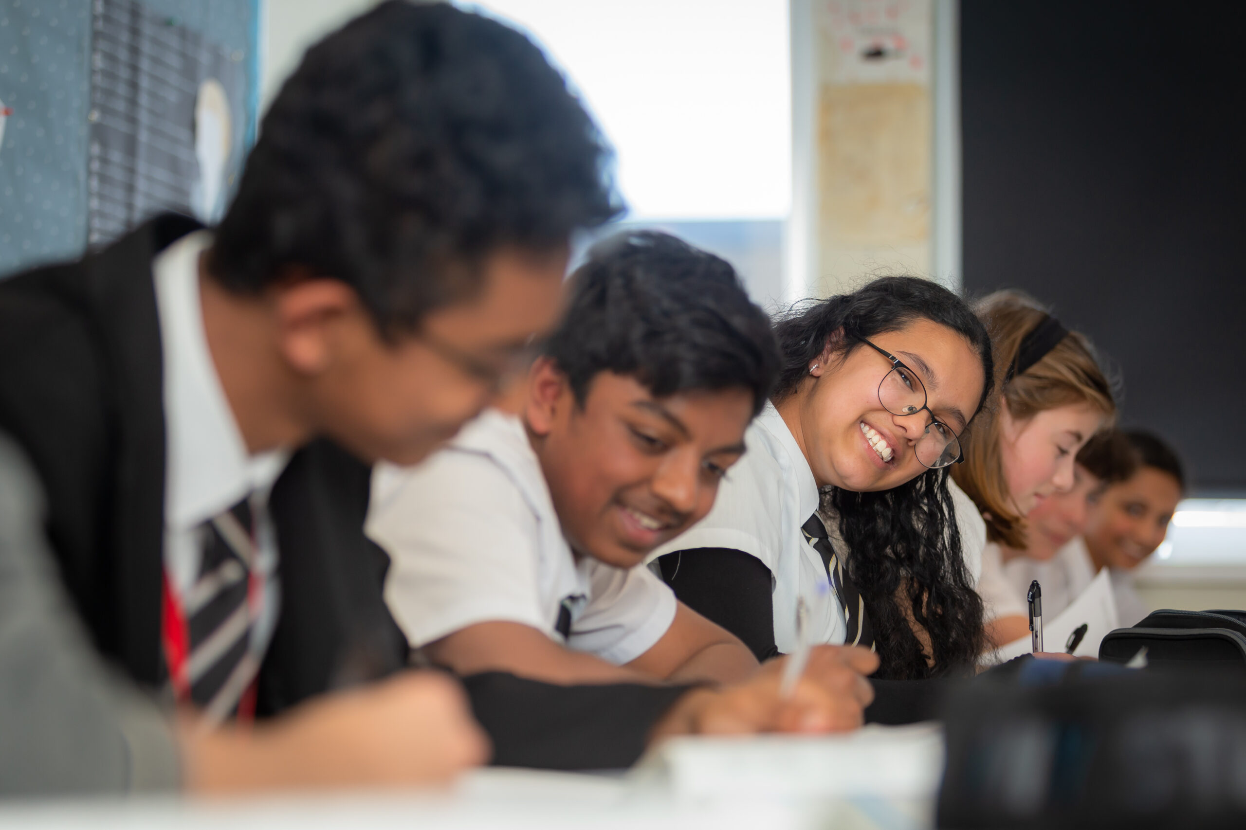 Students in school uniform smiling while working on laptops in classroom