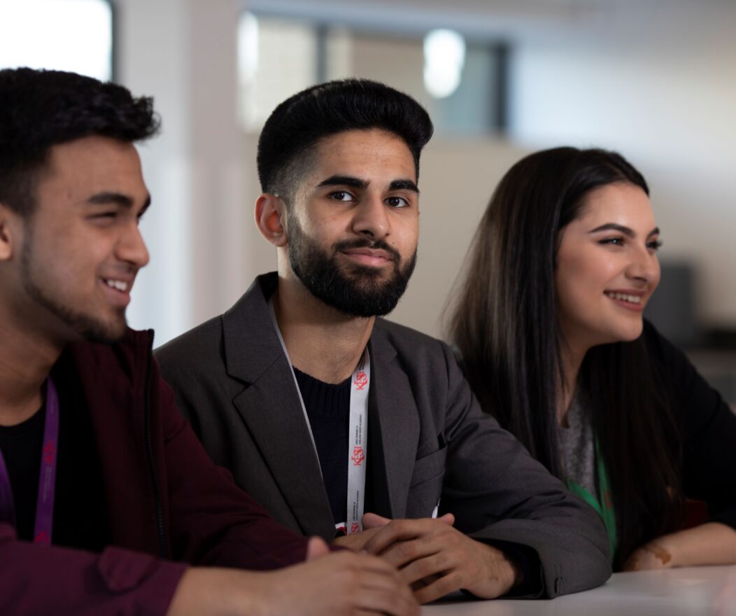 Three students sitting at a table in a classroom setting, engaged in an educational activity.