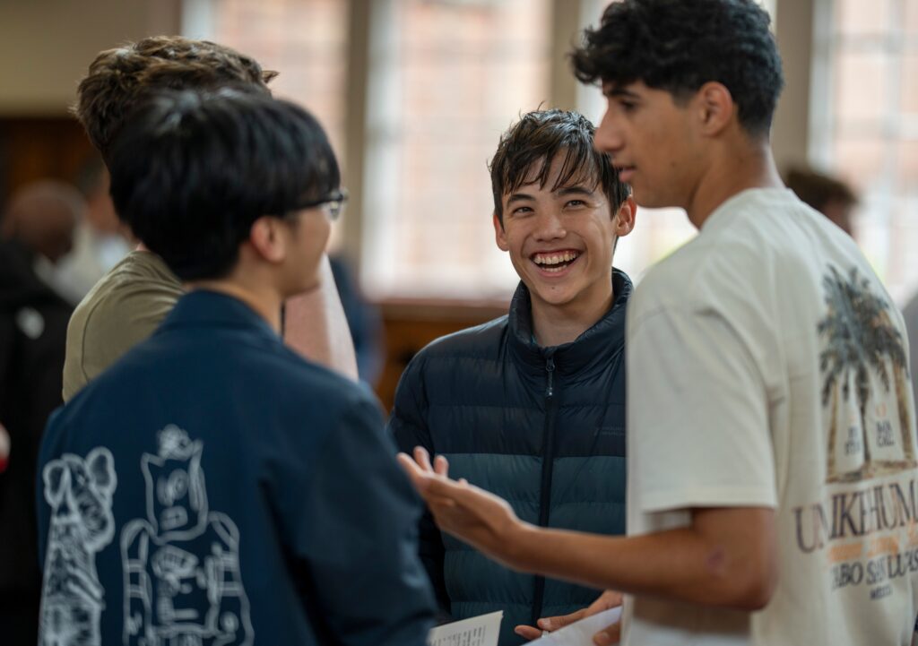 Three students engaged in conversation, smiling and interacting in an educational setting, promoting student life and campus community.