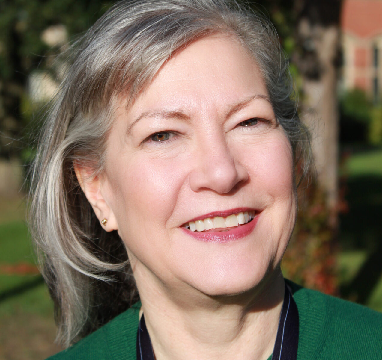 Portrait of a smiling woman with grey hair wearing a green top and lanyard, symbolising educational diversity and professionalism.