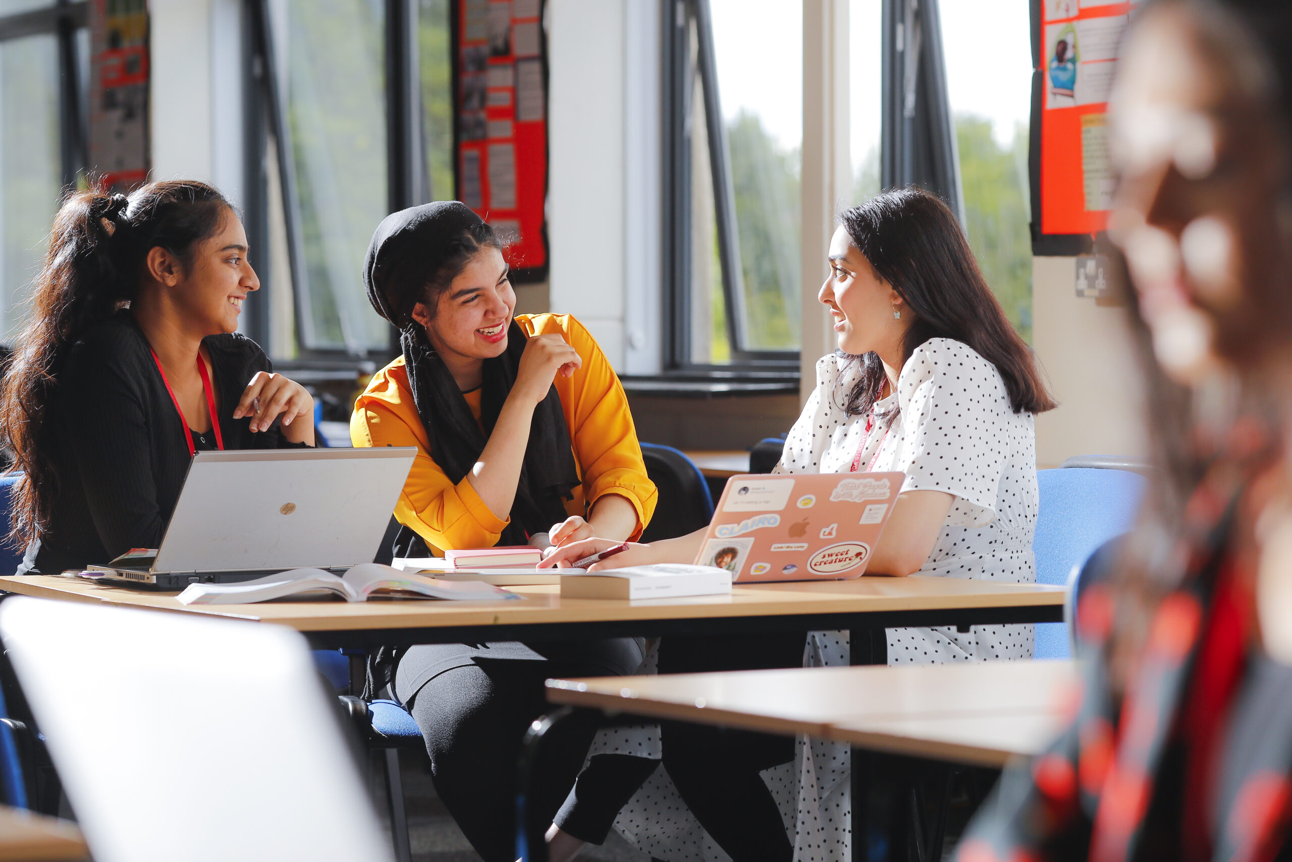 Kevi Foundation students collaborate on a group project in a bright campus workspace, discussing notes and using laptops.